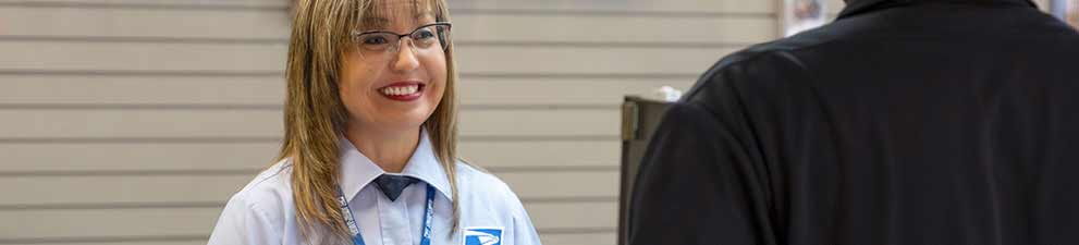 USPS retail associate selling products and services at the Post Office counter.