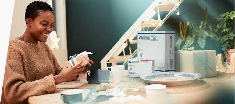 A woman prepares to pack and ship a holiday gift in a Priority Mail box.