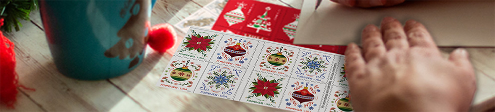 A person addressing a letter with First-Class Mail Forever® holiday stamps on the table.