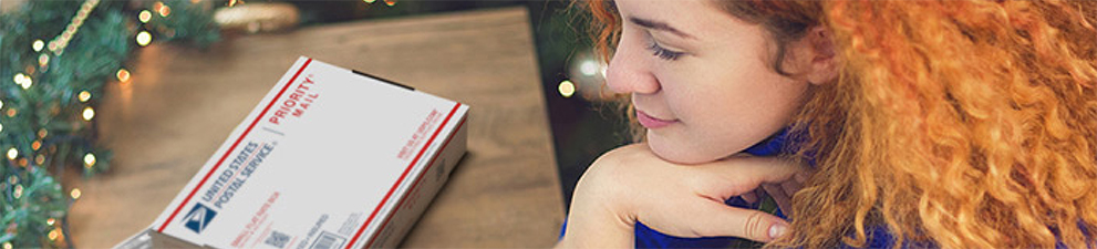 Woman on laptop with Priority Mail box and printed shipping label on the table next to her.